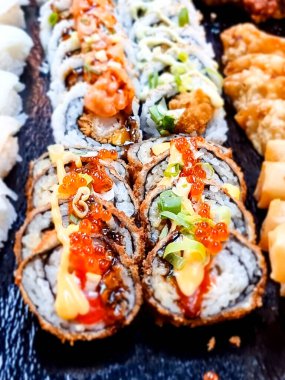 Japon suşisi masada, siyah taş tabakta çeşitli suşi parçaları var.