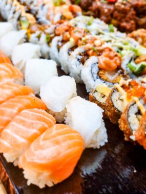 Japon suşisi masada, siyah taş tabakta çeşitli suşi parçaları var.