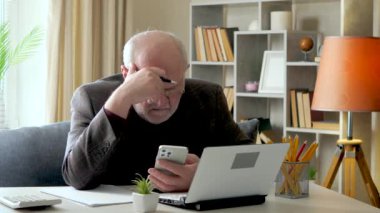 Yaşlı bir işadamı, ceketli, masasında, muhasebe raporundan veri okuyor, yorgun ve uyuyor, çalışanlarla telefon kullanarak iletişim kuruyor. Yavaş çekim