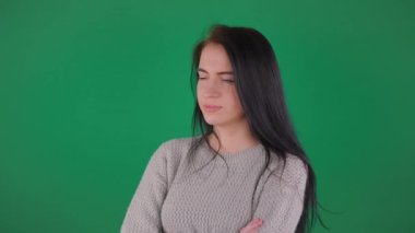 Genç ve güzel bir kız, uzun dalgalı saçlı, düşünceli bir şekilde uzaklığa bakıyor, sallanıyor, huzuru ifade ediyor ve tatlı tatlı gülümsüyor. Yeşil arka plan. Yavaş çekim.