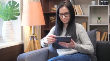 Gözlüklü, uzun siyah saçlı güzel bir kız evdeki kanepede oturan bir tablette bilgi arıyor. Yavaş çekim