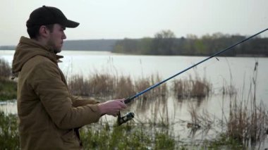 Genç bir adam nehirde balık tutuyor. Mavi gökyüzünün arka planında, doğada, balıkçı balıkları gagalarken izler ve doğayla iletişim kurma zevkine erişir..