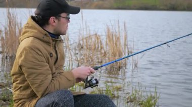 Genç bir adam nehirde balık tutuyor. Mavi gökyüzünün arka planında, doğada, balıkçı balıkları gagalarken izler ve doğayla iletişim kurma zevkine erişir..