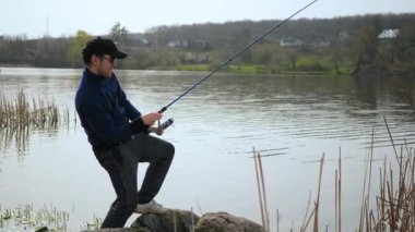 Genç bir adam nehirde balık tutuyor. Mavi gökyüzünün arka planında, doğada, balıkçı balıkları gagalarken izler ve doğayla iletişim kurma zevkine erişir..