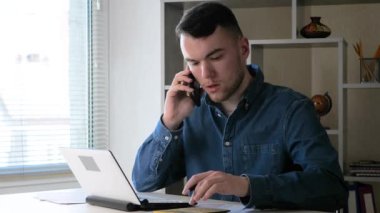 Bilgisayar ve telefon üzerinde çalışan genç bir adam, bir iş adamı, bir muhasebe raporunun verilerini netleştirir, duygusal olarak ifade eder. Evden uzak çalışma.