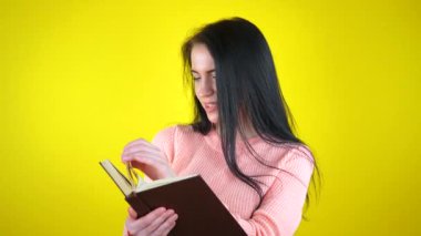 Avrupa görünümlü genç, güzel bir kız, sayfaları karıştırıyor ve kitap okuyor, gülümsüyor. Sarı arkaplan.