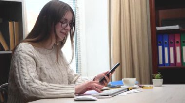 Genç, güzel bir kız yönetici, gözlük takıyor, masasında oturuyor, bir muhasebe raporu hazırlıyor, telefondan veri okuyor ve bilgisayara giriyor..