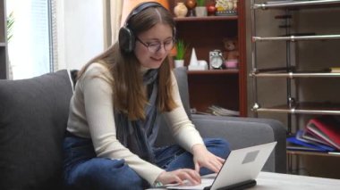 Genç, güzel bir kız, gözlüklü beyaz bir bluz içinde, rahat bir ev ortamında kanepede oturuyor, müzik dinliyor, bilgisayarına e-posta yazıyor ve gülümsüyor. Yavaş çekim.