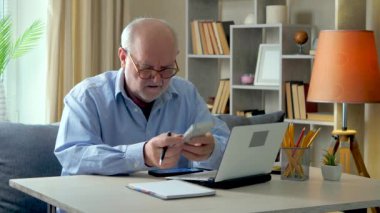 Mavi gömlek giyen, gözlüklü yaşlı bir adam yıllık muhasebe raporu üzerinde çalışıyor, telefonla konuşuyor, bilgisayardaki verileri kontrol ediyor, bir belgeye yazıyor. Evden çalışıyorum. Yavaş