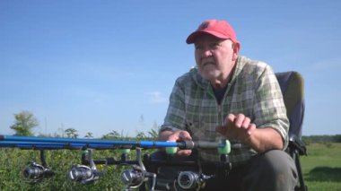 Kırmızı beyzbol şapkası ve gözlük takan yaşlı bir adam balık tutuyor, doğal koşullarda balık tutuyor. Balıkları oltaya getirir. Yavaş Hareket