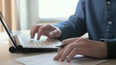 Ofiste, iş yapmak için eşyalarla dolu bir masada yakın plan bir iş adamının elleri. Bir iş adamı bir hesap makinesi ve bir bilgisayar kullanarak küresel bir mali raporun verilerini hesaplar. Yavaş çekim.