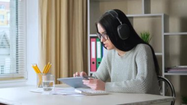  Gözlüklü ve kulaklıklı genç bir kız, bir öğrenci, arkadaşlarıyla telefon ve bilgisayar kullanarak iletişim kuruyor, duygusal olarak hareket ediyor ve ekranda gülümsüyor. Yavaş Hareket