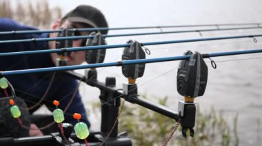 Mavi ceketli, gözlüklü genç bir adam, bir olta kamışını, nehrin kenarında, açık havada, sessizliğin tadını çıkararak ve iyi bir avın hayalini kurarak, bir ödül balığı yakalama umuduyla manipüle ediyor. Yavaş çekim.