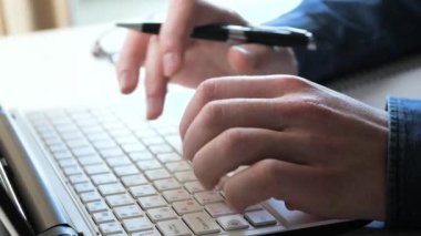 Ofiste, iş yapmak için eşyalarla dolu bir masada yakın plan bir iş adamının elleri. Bir iş adamı bir hesap makinesi ve bir bilgisayar kullanarak küresel bir mali raporun verilerini hesaplar. Yavaş çekim.