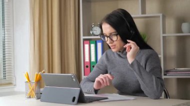 Koyu renk saçlı, gri kazaklı, kulaklıklı genç bir kız öğretmeniyle video bağlantısı üzerinden iletişim kuruyor..