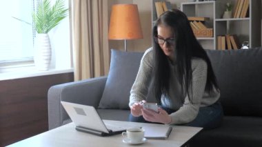 Genç, güzel iş kadını çalışıyor, bilgisayar teknolojisi kullanıyor, evde otururken internet sayfalarını karıştırıyor, iş raporlarında düzeltmeler yapıyor ve düzeltmeler yapıyor..