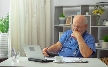 Yaşlı bir adam, bir doktor, ofisinde, bir masada..
