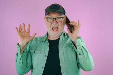 Ellerinde telefon olan yaşlı bir adam. Pembe arkaplan.