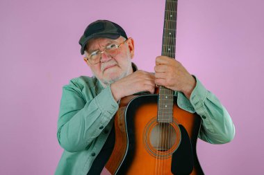 Elinde gitarla yaşlı bir adam. Pembe arkaplan.