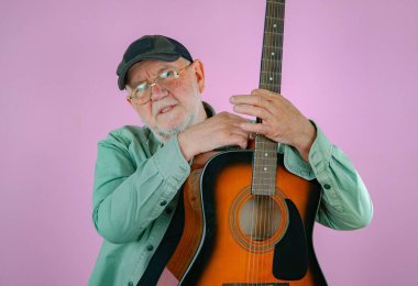 Elinde gitarla yaşlı bir adam. Pembe arkaplan.