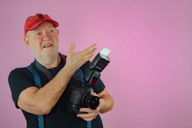 Elinde kamera olan yaşlı bir adam, bir fotoğrafçı. Pembe arkaplan.