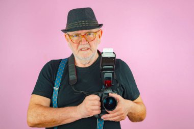 Elinde kamera olan yaşlı bir adam, bir fotoğrafçı. Pembe arkaplan.