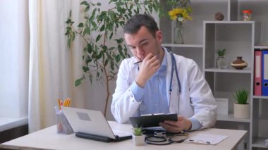 Genç bir stajyer doktor bir ofiste çalışıyor, tedavi yöntemlerini ve teşhisi hastanın tıbbi geçmişine yazıyor. Yavaş çekim.