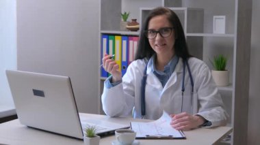 Genç, güzel bir bayan doktor ofisinde bilgisayarında çalışıyor, hastanın sağlık bilgilerini kontrol ediyor ve hastanın durumu hakkında konuşuyor. Yavaş çekim.
