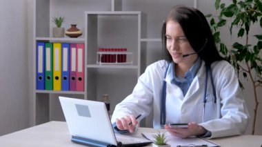 Genç, güzel bir doktor bilgisayar başında bir ofiste çalışıyor ve akıllı telefonuyla hastanın sağlığıyla ilgili verileri kontrol ediyor ve veri tabanına giriyor..