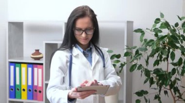 Üzerinde teleskop olan genç ve güzel bir doktor hastanın tıbbi geçmişine bir tabletle bakıyor ve hastaya hangi tedaviyi yazacağına karar veriyor. Yavaş çekim.