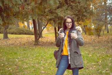 Genç, güzel bir kız doğada seyahat eder, sonbahar ormanının güzelliğine hayranlıkla hayran olur, fotoğraf çeker, not alır, gülümser, eğlenir..