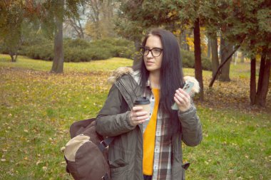 Genç, güzel bir kız doğada seyahat eder, sonbahar ormanının güzelliğine hayranlıkla hayran olur, fotoğraf çeker, not alır, gülümser, eğlenir..