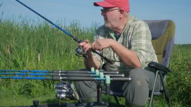 Yaşlı bir balıkçı sporla meşgul, doğanın tadını çıkarıyor, güneşli bir gün, su köpüğü ve uzun zamandır beklenen balık ısırığı. Yavaş çekim.