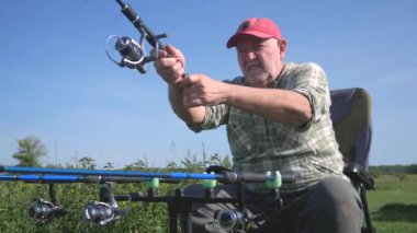 Yaşlı bir balıkçı sporla meşgul, doğanın tadını çıkarıyor, güneşli bir gün, su köpüğü ve uzun zamandır beklenen balık ısırığı. Yavaş çekim.
