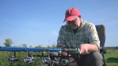 Yaşlı bir balıkçı sporla meşgul, doğanın tadını çıkarıyor, güneşli bir gün, su köpüğü ve uzun zamandır beklenen balık ısırığı. Yavaş çekim.