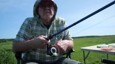 Yaşlı bir balıkçı sporla meşgul, doğanın tadını çıkarıyor, güneşli bir gün, su köpüğü ve uzun zamandır beklenen balık ısırığı. Yavaş çekim.