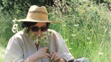 Orta yaşlı bir çiftçi kadın, güneşli bir yaz gününde açık havada, bir buket yabani çiçeğin, papatyanın, gülümsemenin tadını çıkarıyor. Yavaş çekim.