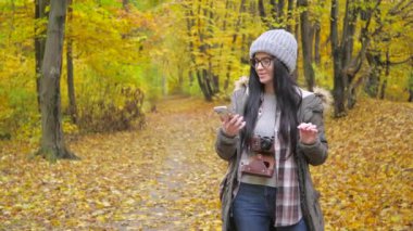 Doğada seyahat. Sonbahar ormanlarında genç ve güzel bir kız sonbahar doğasının güzelliklerinden zevk alır, GPS ile telefon kullanır, gülümser. Yavaş çekim.