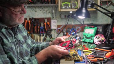 Yaşlı bir teknisyen, ölçüm aletleri ve teknik aletlerle atölyede bilgisayar donanımı tamir ediyor. Yavaş çekim.