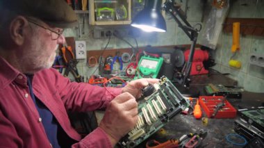 Yaşlı bir teknisyen, ölçüm aletleri ve teknik aletlerle atölyede bilgisayar donanımı tamir ediyor. Yavaş çekim.