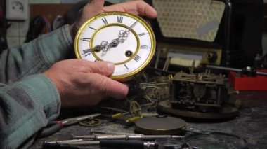 Yaşlı bir zanaatkar, atölyede eski bir saat mekanizmasını, antika bir saati tamir eder, dişlileri yağlar, tozdan ve çamurdan temizler. Yavaş çekim.