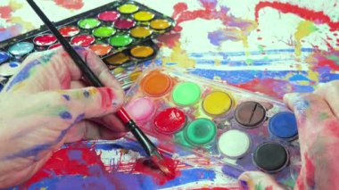 Sanatçının elleri, sanatta yaratıcı imgeler yaratmak için çalışır. Resim boyaları ve fırçalar, palet, guaj ve suluboya kullanarak tuvale çok renkli dokunuşlar uyguluyorlar..