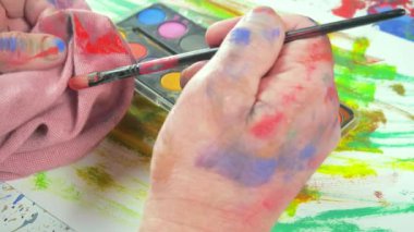 Sanatçının elleri, sanatta yaratıcı imgeler yaratmak için çalışır. Resim boyaları ve fırçalar, palet, guaj ve suluboya kullanarak tuvale çok renkli dokunuşlar uyguluyorlar..