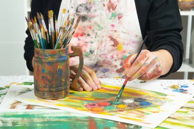 Boya paleti ve fırçalarla sanatçıların ellerine yakın çekim.