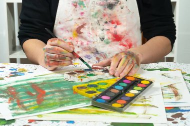 Boya paleti ve fırçalarla sanatçıların ellerine yakın çekim.