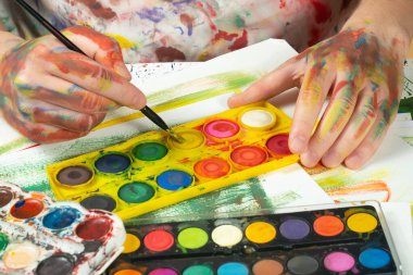 Boya paleti ve fırçalarla sanatçıların ellerine yakın çekim.