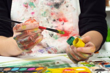 Boya paleti ve fırçalarla sanatçıların ellerine yakın çekim.