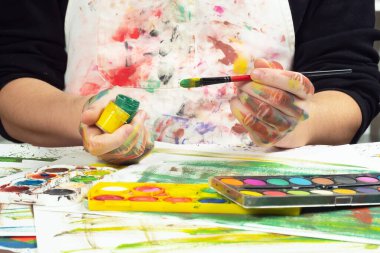 Boya paleti ve fırçalarla sanatçıların ellerine yakın çekim.