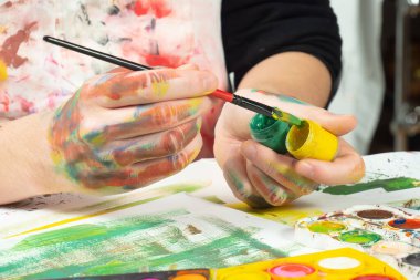 Boya paleti ve fırçalarla sanatçıların ellerine yakın çekim.