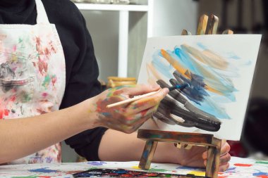 Boya paleti ve fırçalarla sanatçıların ellerine yakın çekim.